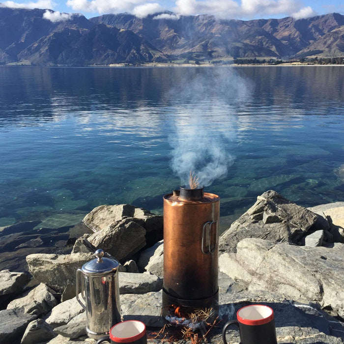 Why the Thermette Kettle is the Ultimate Outdoor Icon on a lakeside with coffee mugs and majestic mountains in the background.