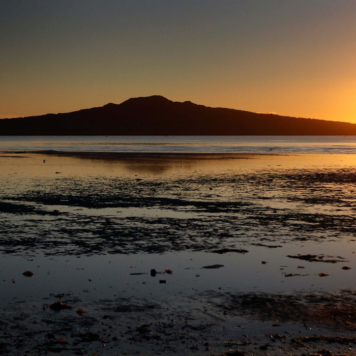 Sunset over a calm bay reflecting a mountain, showcasing serene nature and coastal beauty.