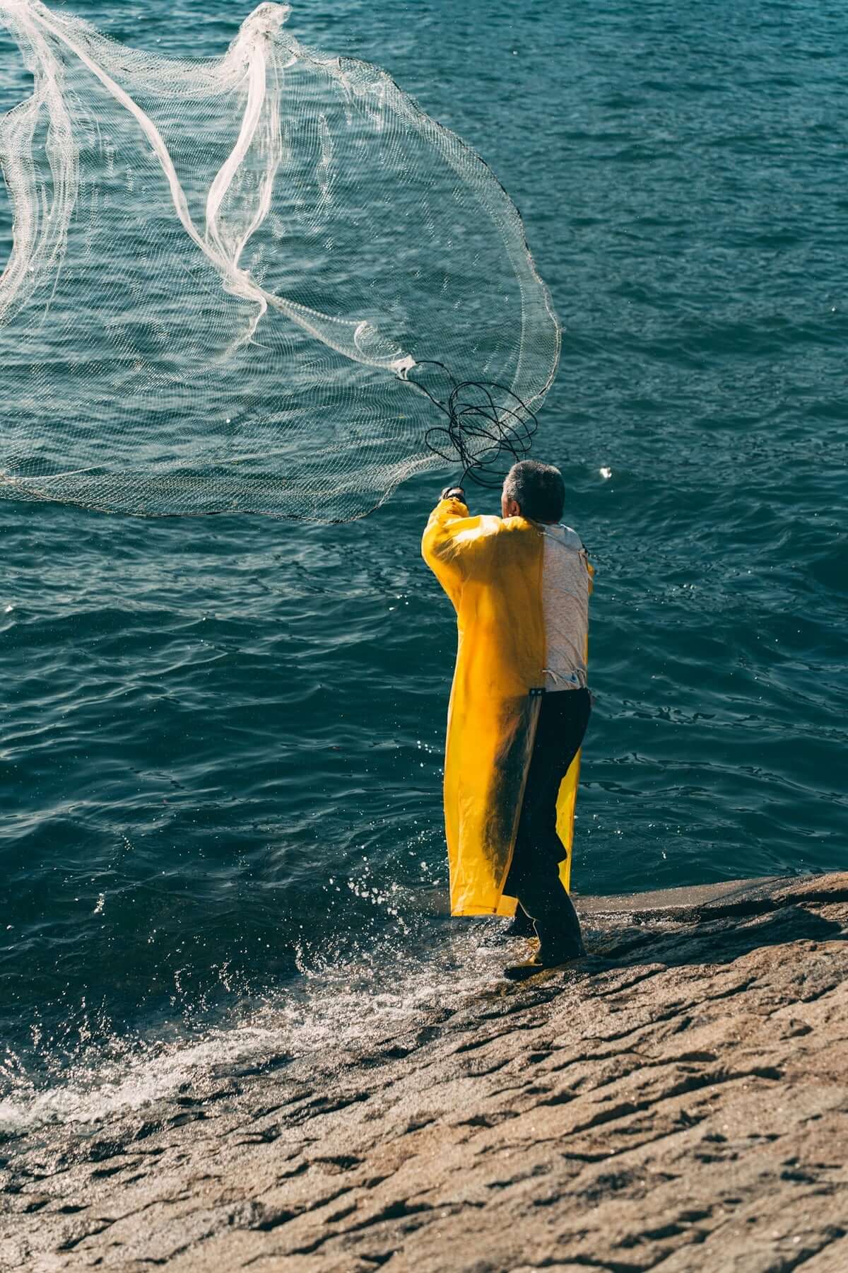 Person casting a Heavy-Duty Bait Drag Nets into the water from a rocky shore.
