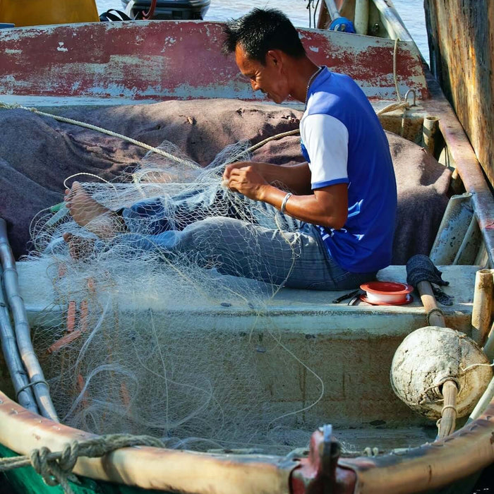 A fisherman on a boat working with dark green long line twine while repairing fishing nets.
