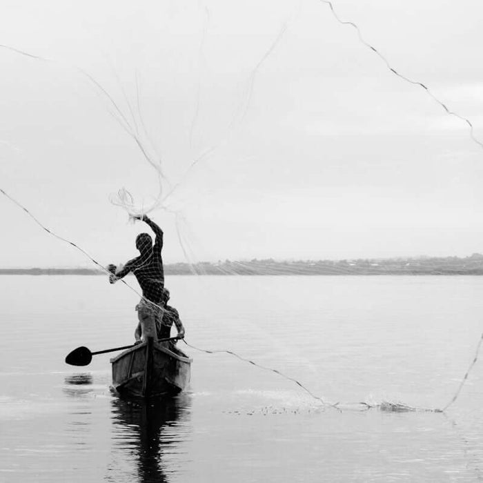 grayscale photography of person in boat throwing fishing net
