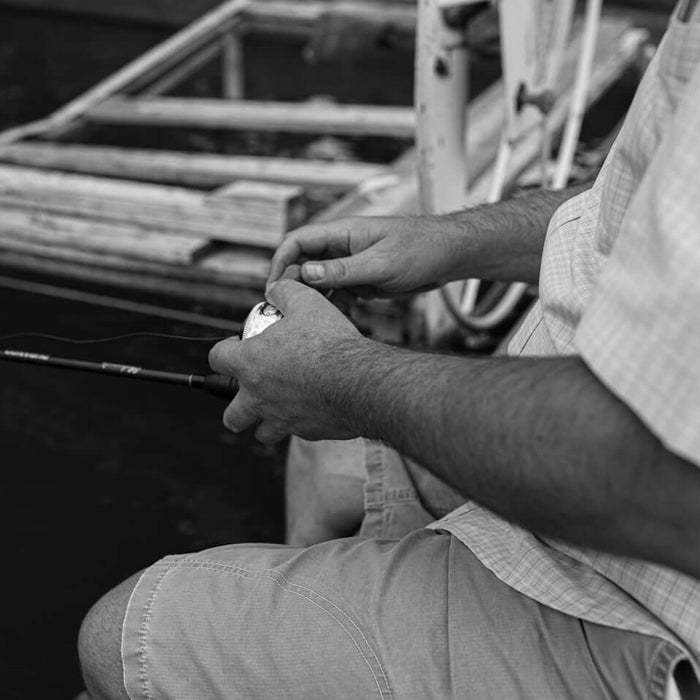 Fishing enthusiast preparing bait cotton in fishing tactics on a boat by the water.