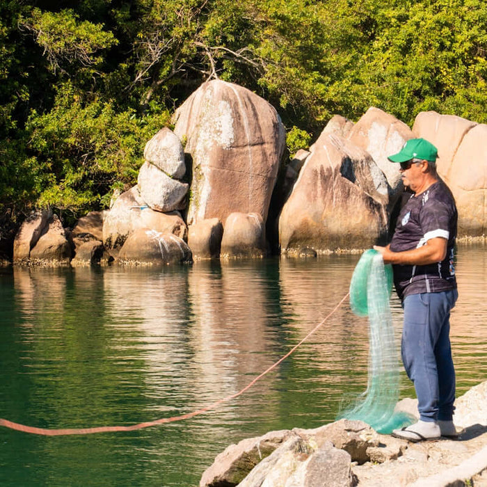 A man fishing near water using a 60m Fishing Net Buoy Anchor 2.5kg Dan Combo.