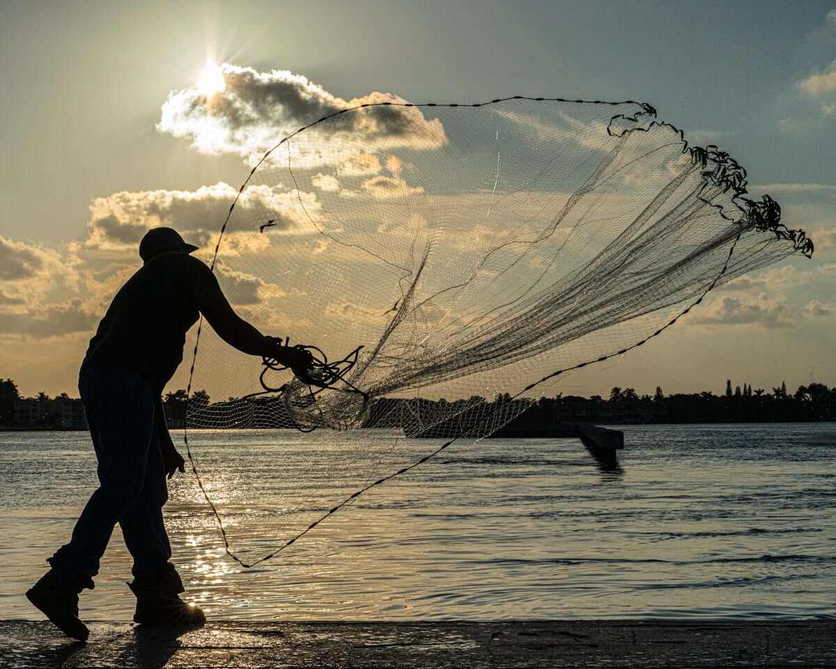 Person casting a net while fishing with 3 Inch 0.50mm Pacific Island Fishing Mesh at sunset.