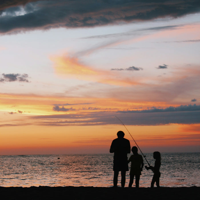 silhouette of children and man standing on shore with fishing rod during golden hour