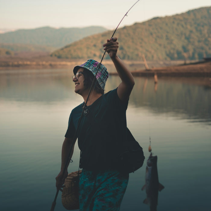 man wearing black shirt holding fishing rod while standing near lake