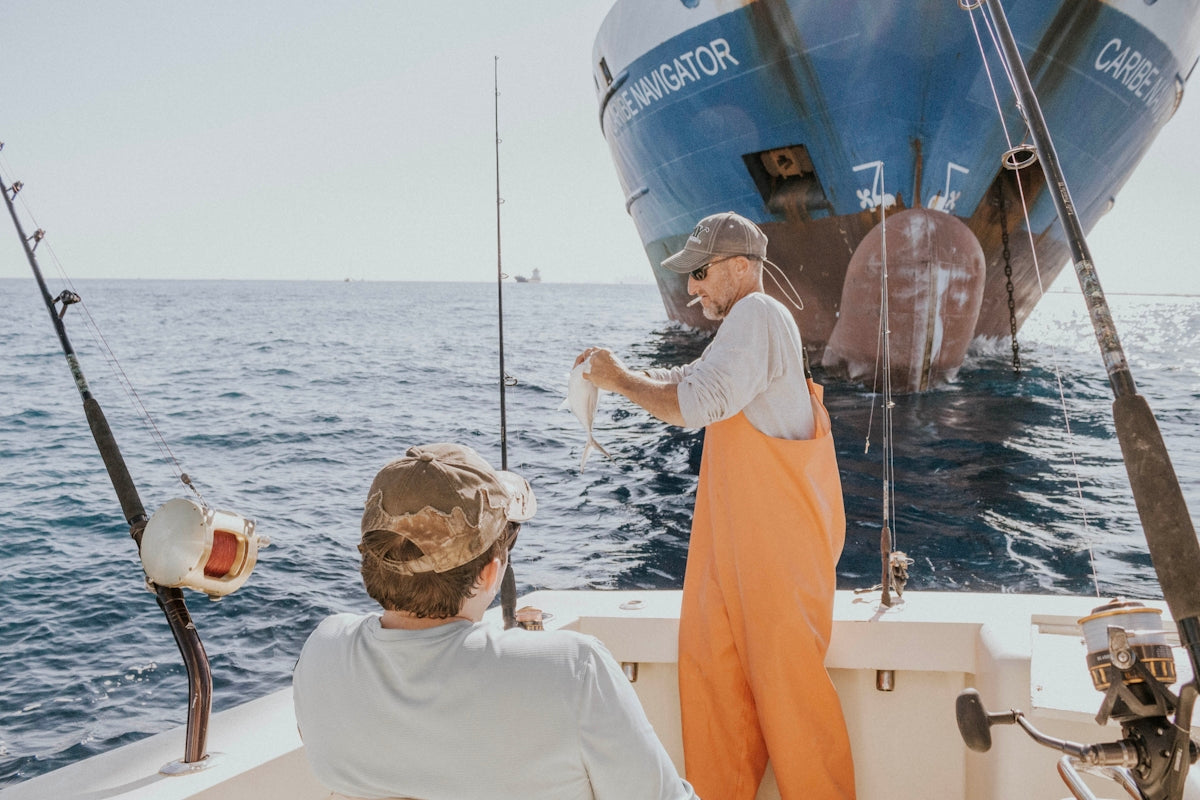 two person in fishing boat near cargo ship during daytime