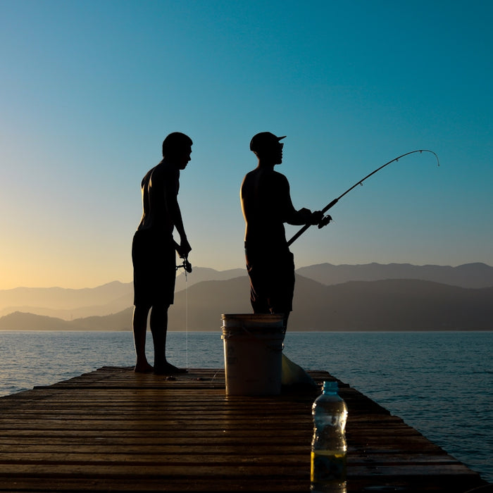 silhouette of man and woman holding fishing rod standing on dock during sunset