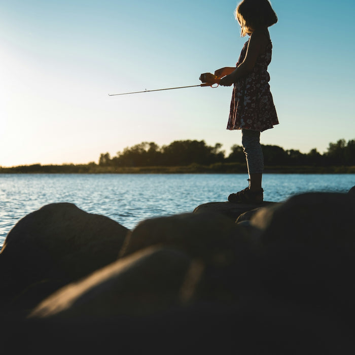 woman in white and black dress holding fishing rod standing on rock near body of water