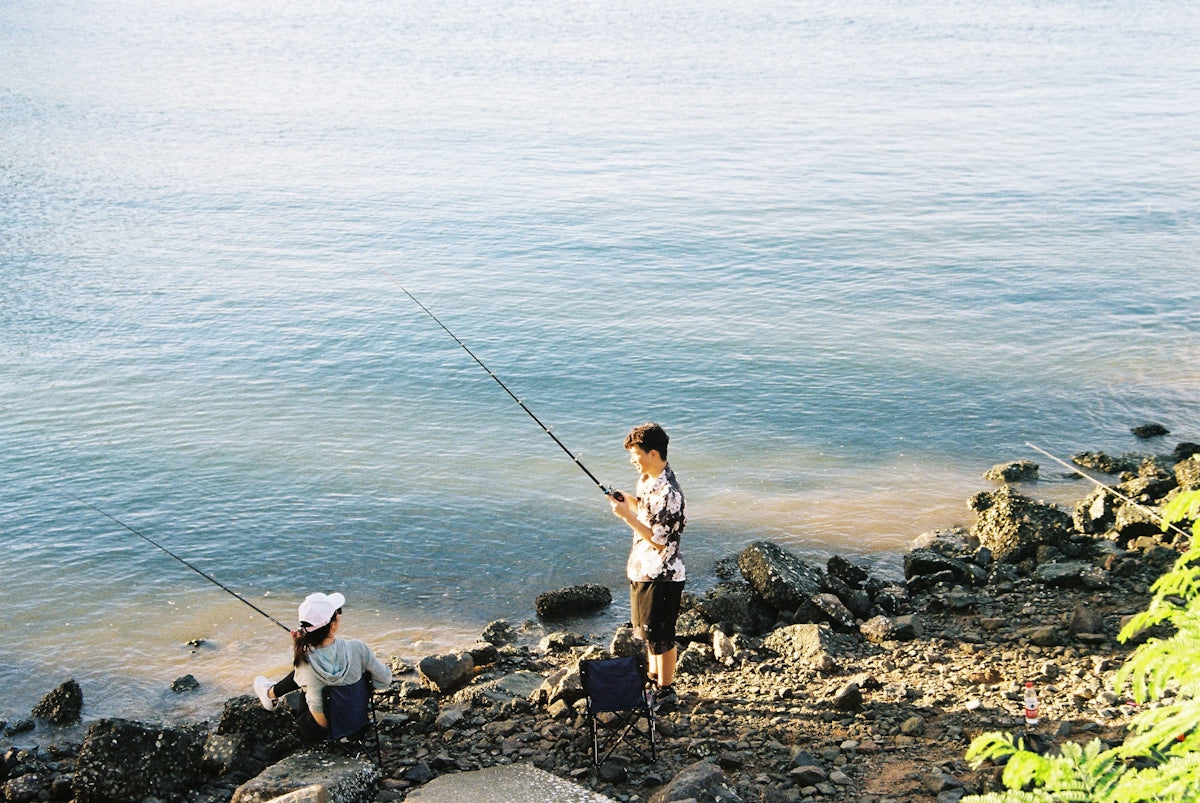 woman in white shirt and black pants fishing on sea during daytime