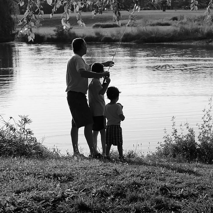a black and white photo of a man and two children by a river