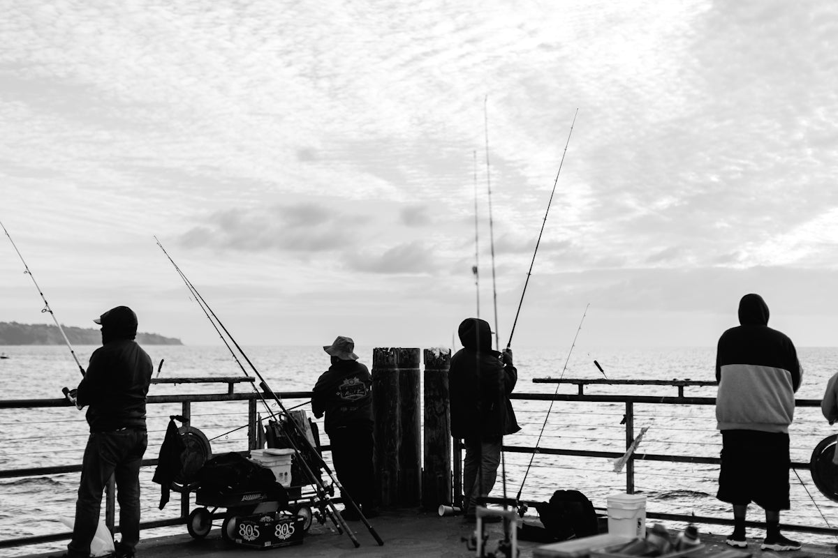 People are fishing off a pier in monochrome.