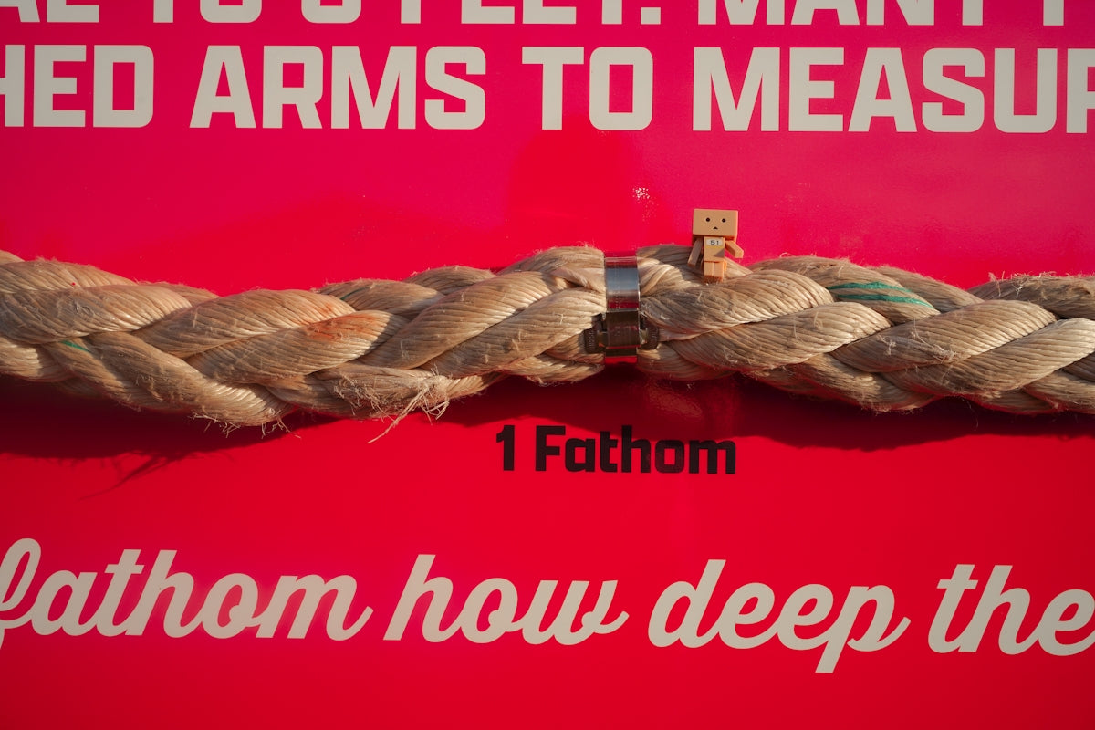 A tiny figure stands on a fathom-measured rope.