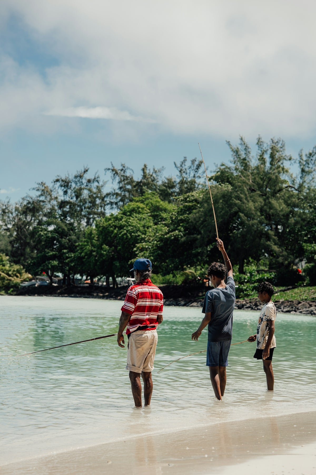 Three people are fishing in the shallow water.