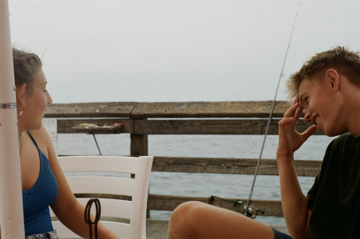 Two people are laughing while sitting on a pier.