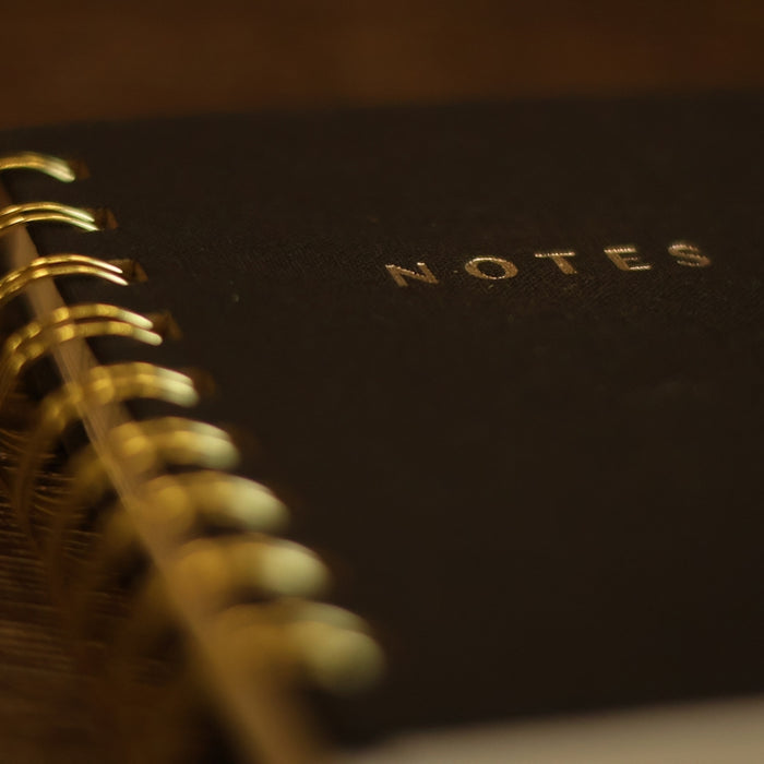 A black notebook with a gold spiral binding.