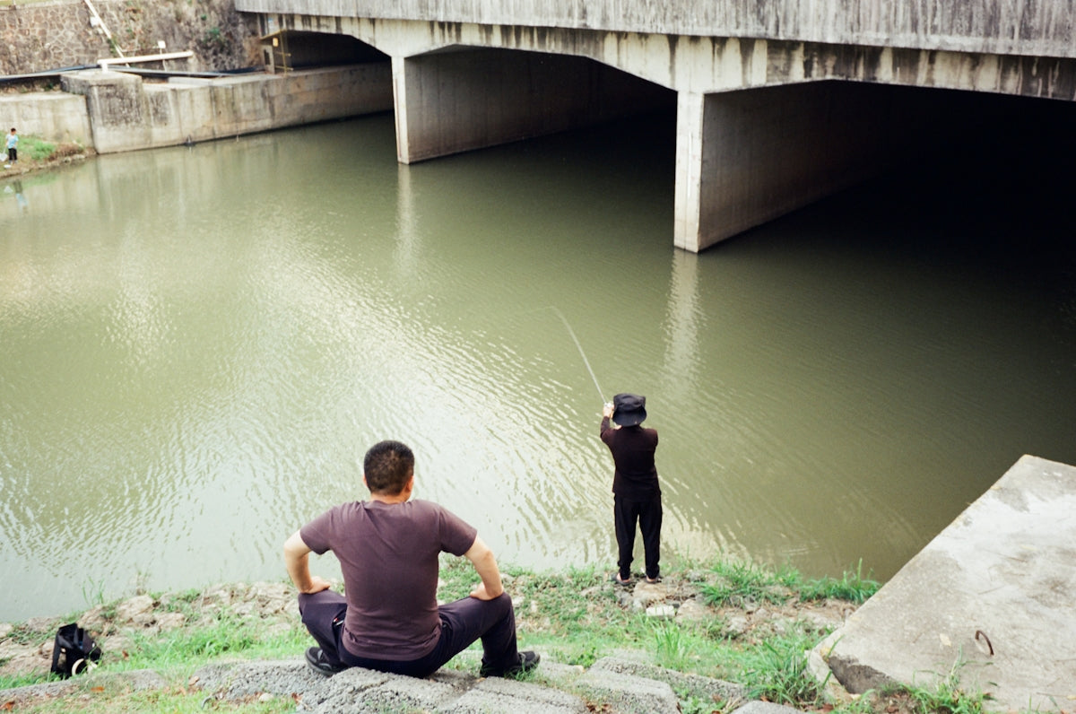 Two people fishing under a concrete bridge.