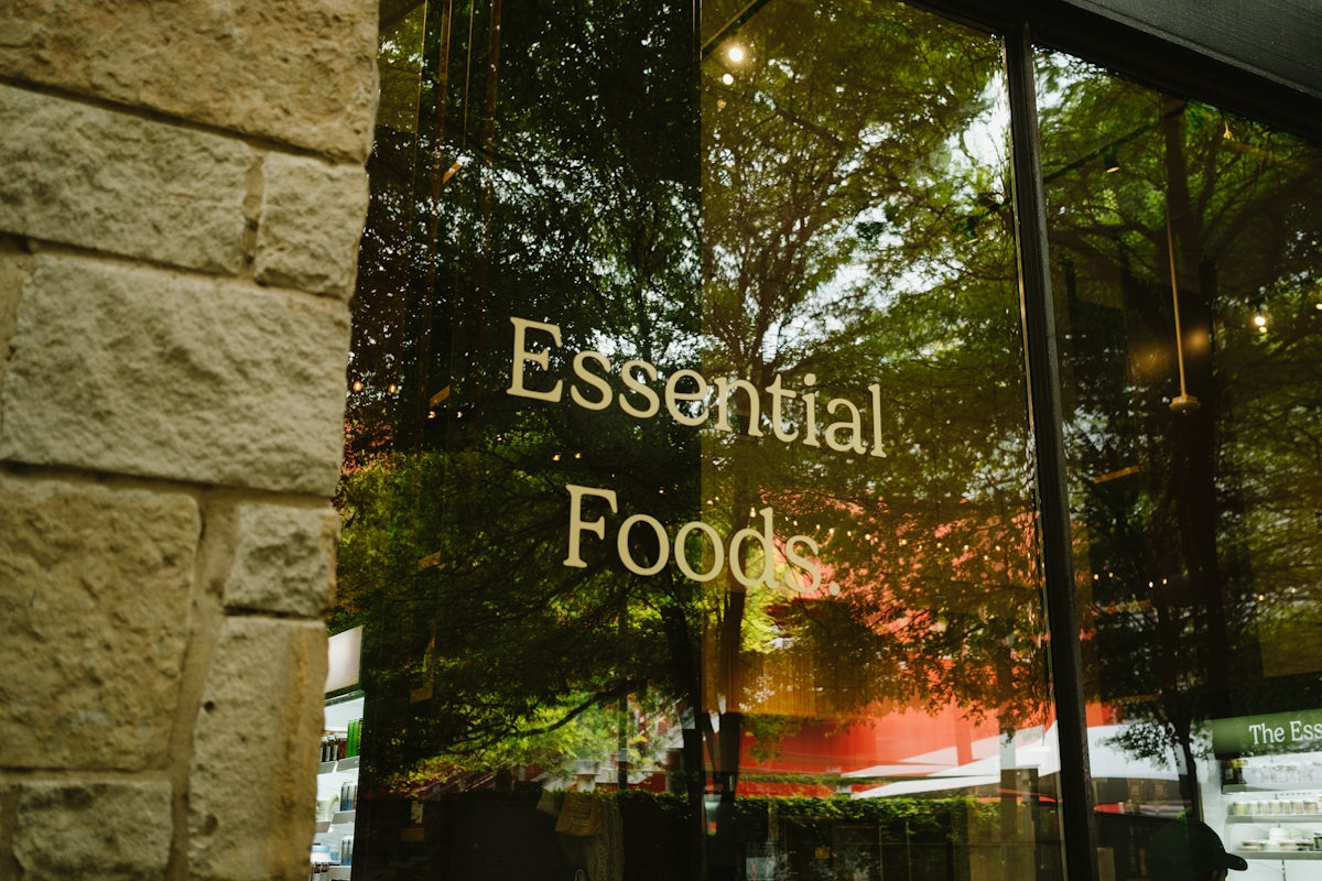 Essential foods sign on a glass window with tree reflections.